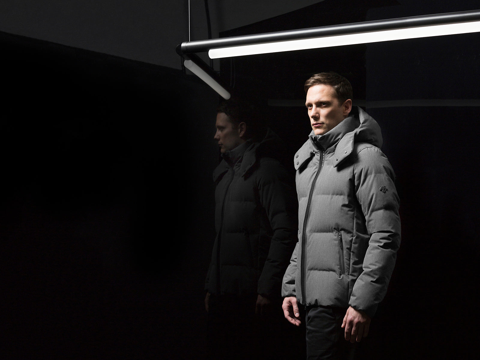 a man in dark clothing standing in a dimly lit room with a light fixture.