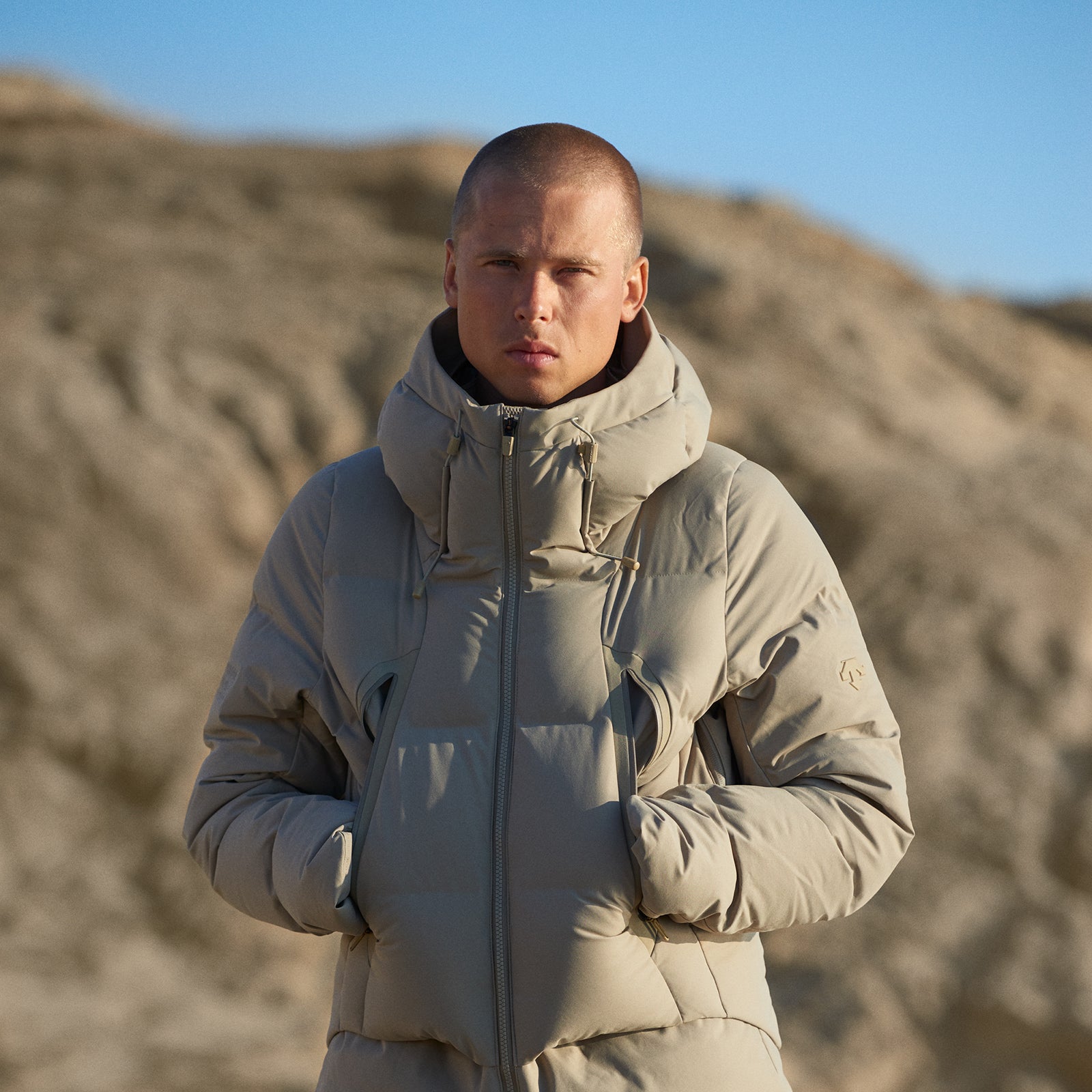 Man wearing a beige puffer jacket standing in a desert landscape